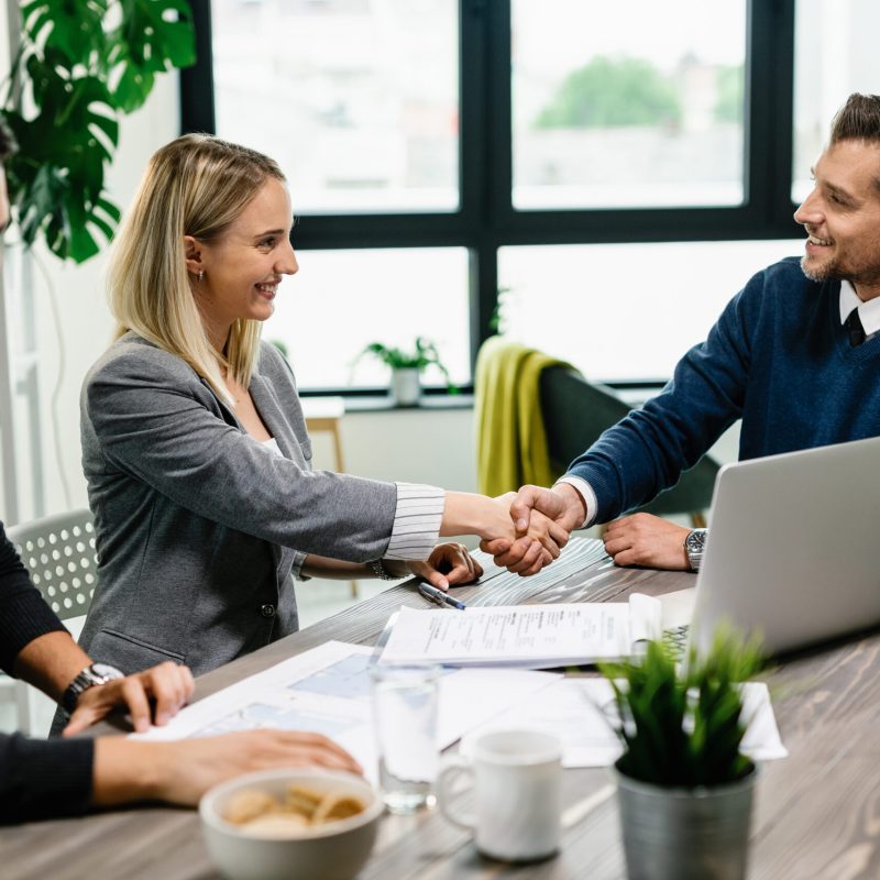 Young happy couple meeting with financial advisor in the office. Woman is handshaking with the agent.